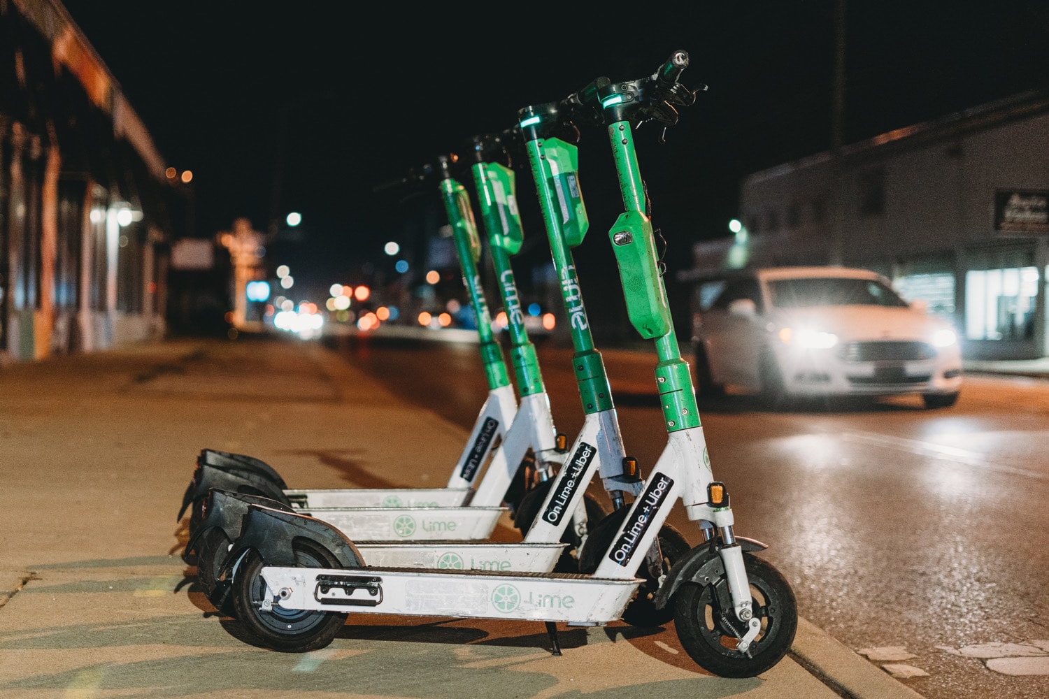 Vier E-Scooter von Lime stehen nebeneinander auf einem Bürgersteig am Abend