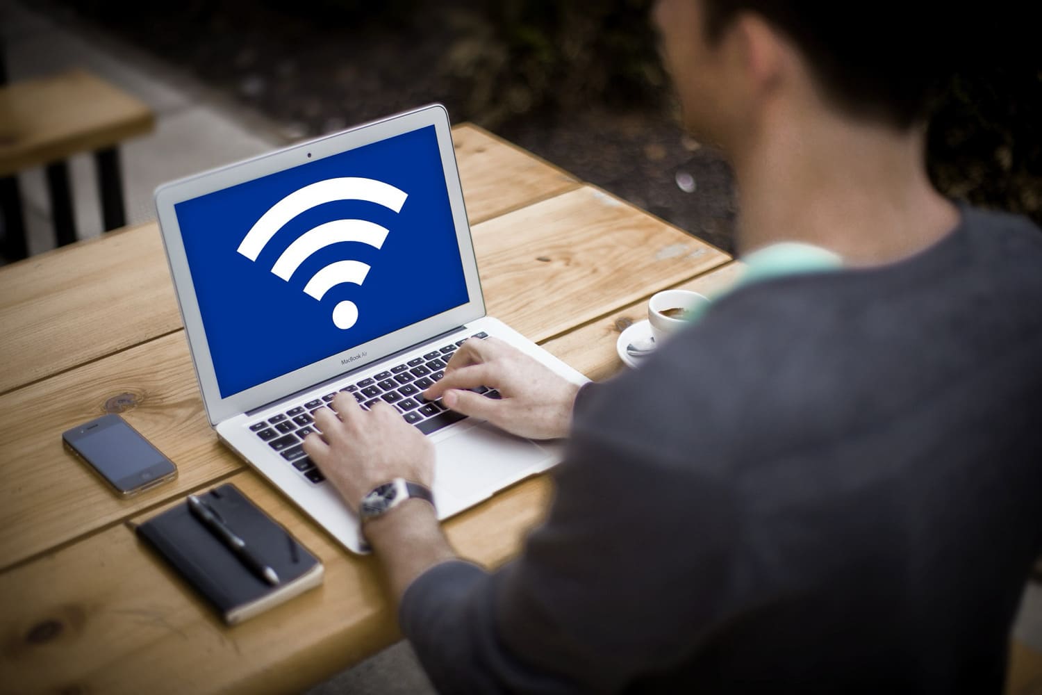 Person sitzt an einem MacBook, auf dem Bildschirm ein großes WLAN-Empfangssymbol