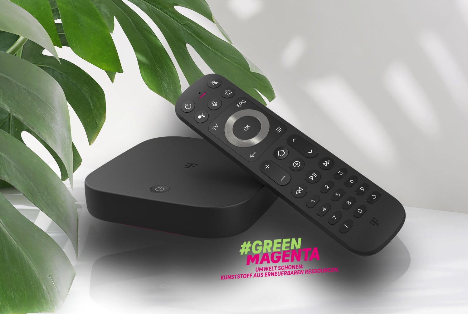 Neue MagentaTV One Box mit Fernbedienung neben einer Grünpflanze