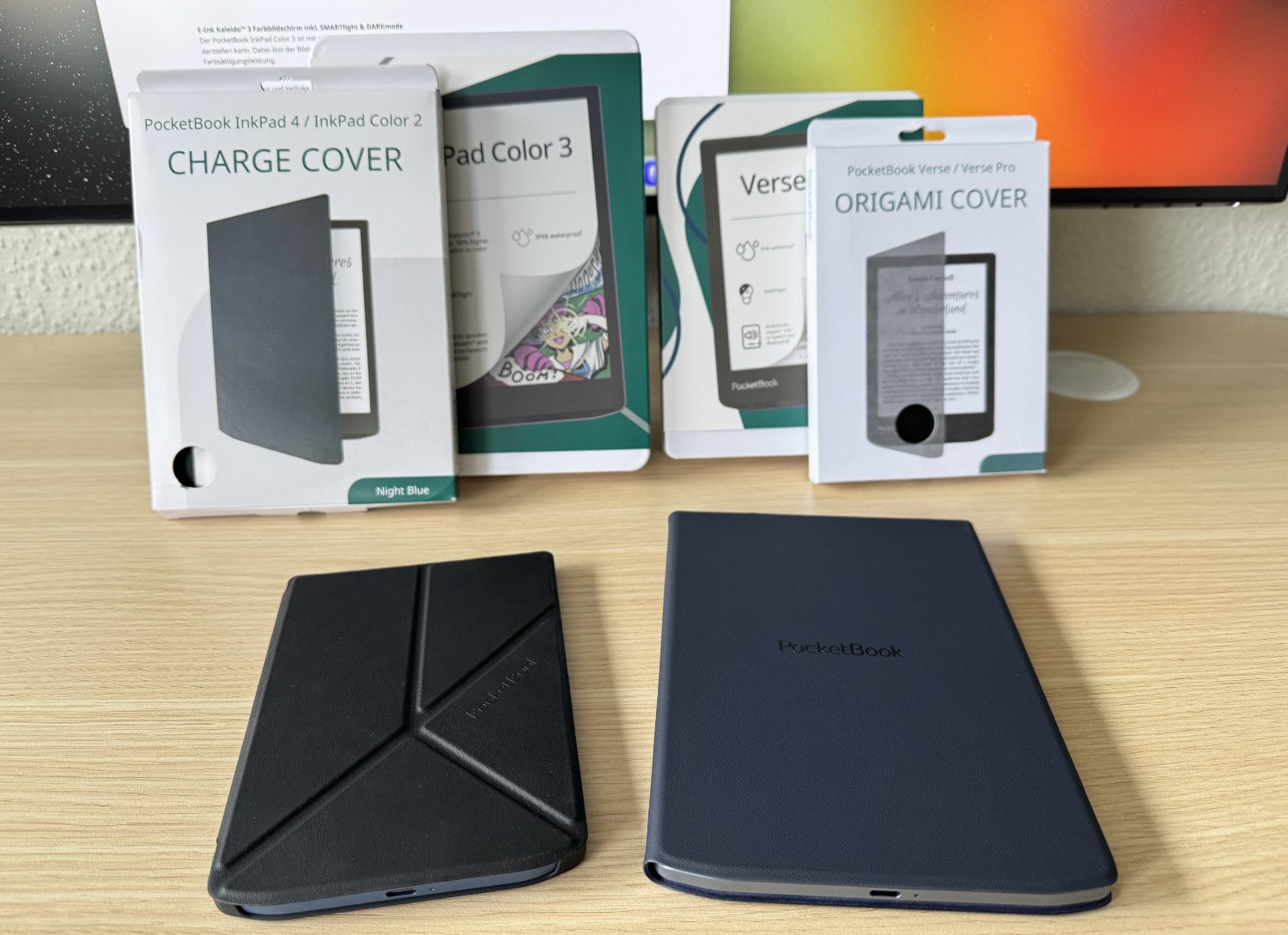 PocketBook InkPad Color 3 und Verse Pro mit Cases und Verpackungen im Hintergrund