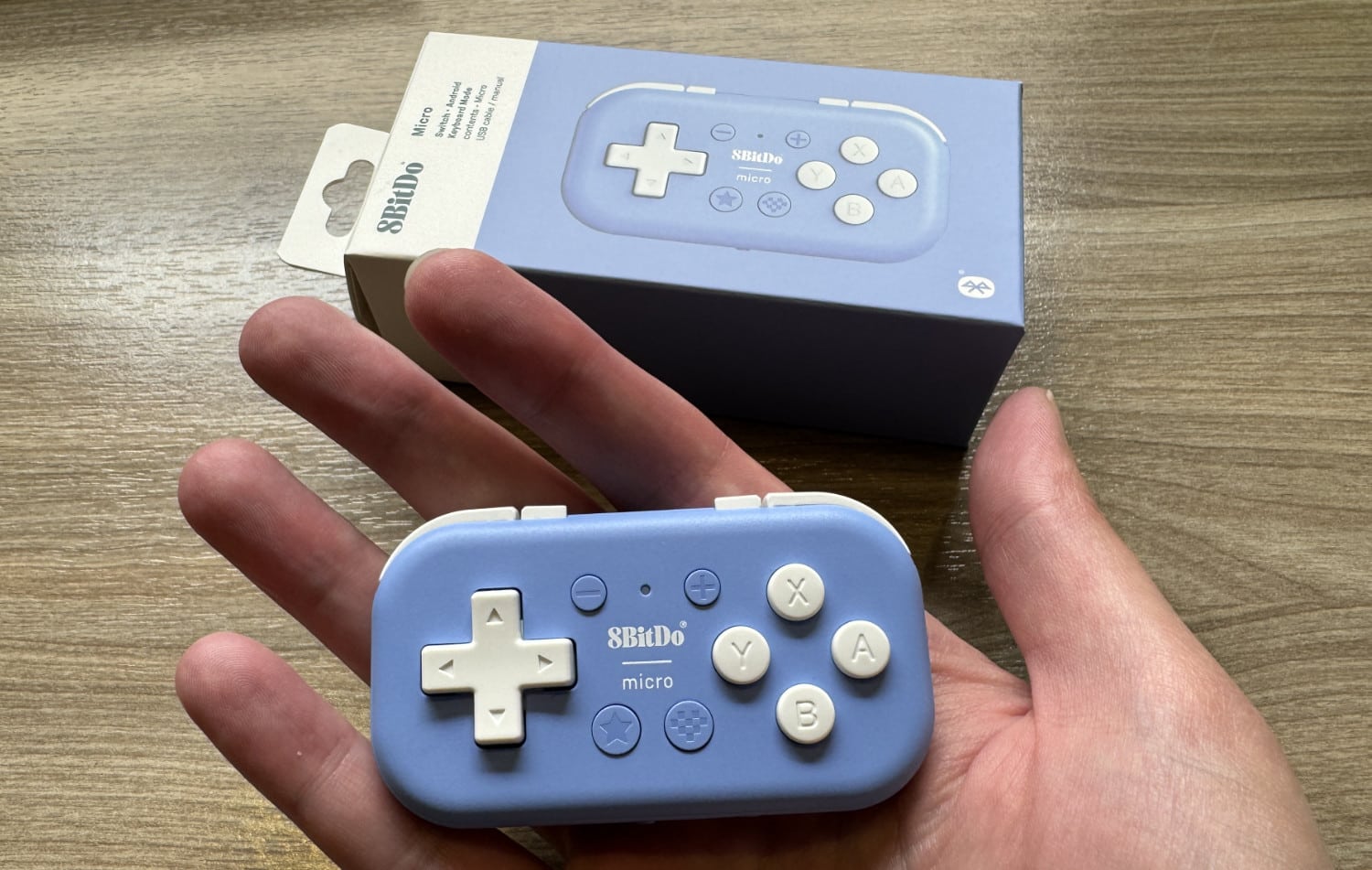 8BitDo Micro in Blau einer Handfläche, dahinter die Verpackung