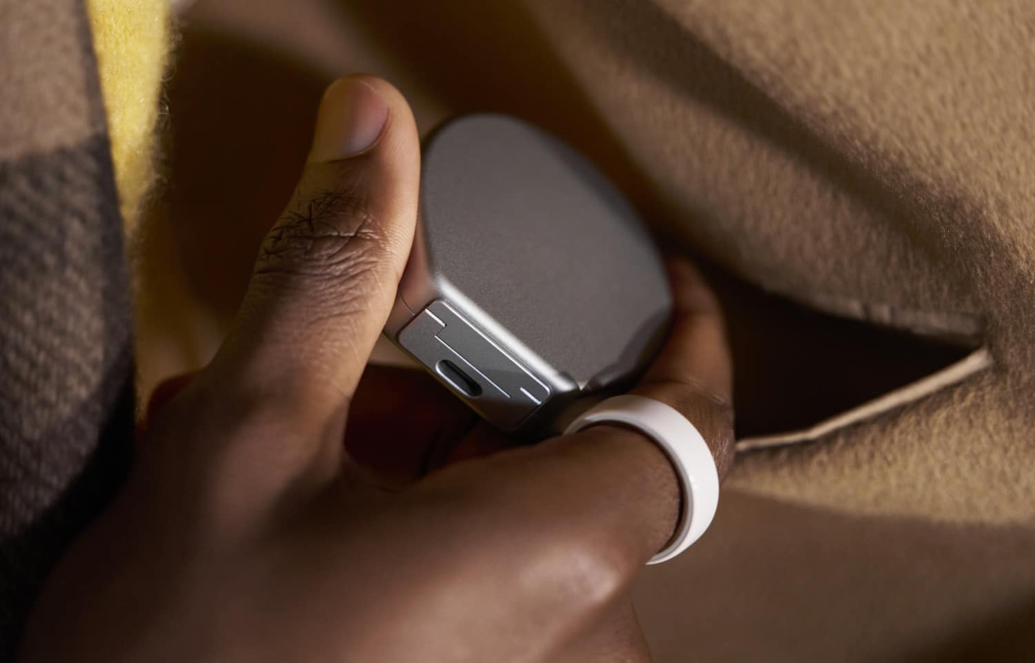 Eine Hand hält das silberfarbene Oura Ring 4 Ladecase, der USB-C-Port auf der Rückseite ist sichtbar